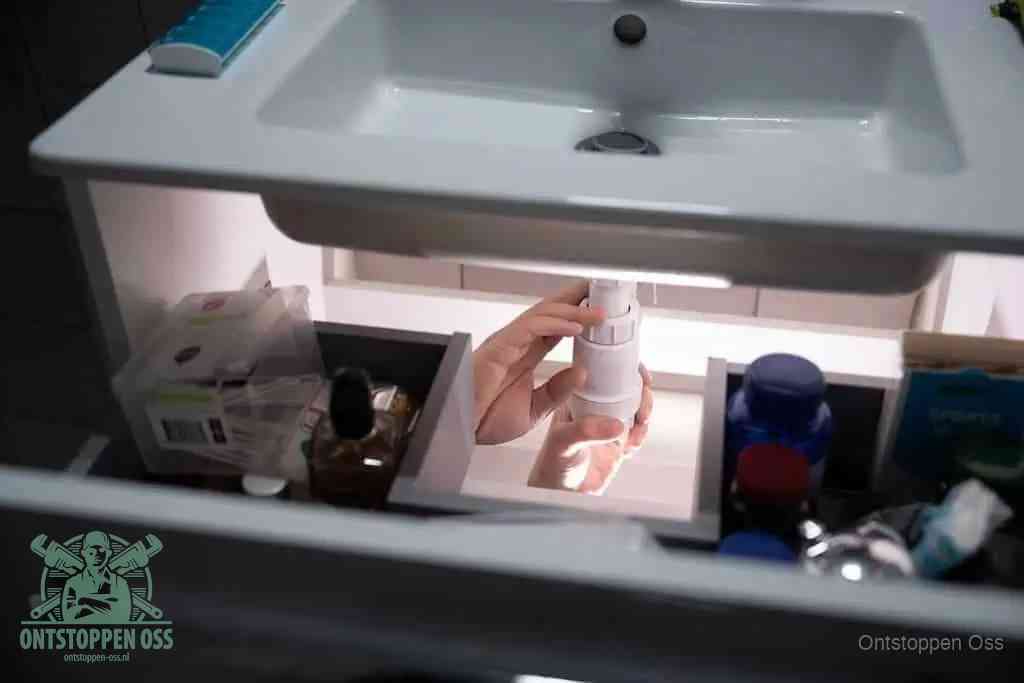 Een pompfles met zeep boven een wastafel, de heet water en afwasmiddel-methode om een vetprop in de afvoer los te maken in Oss