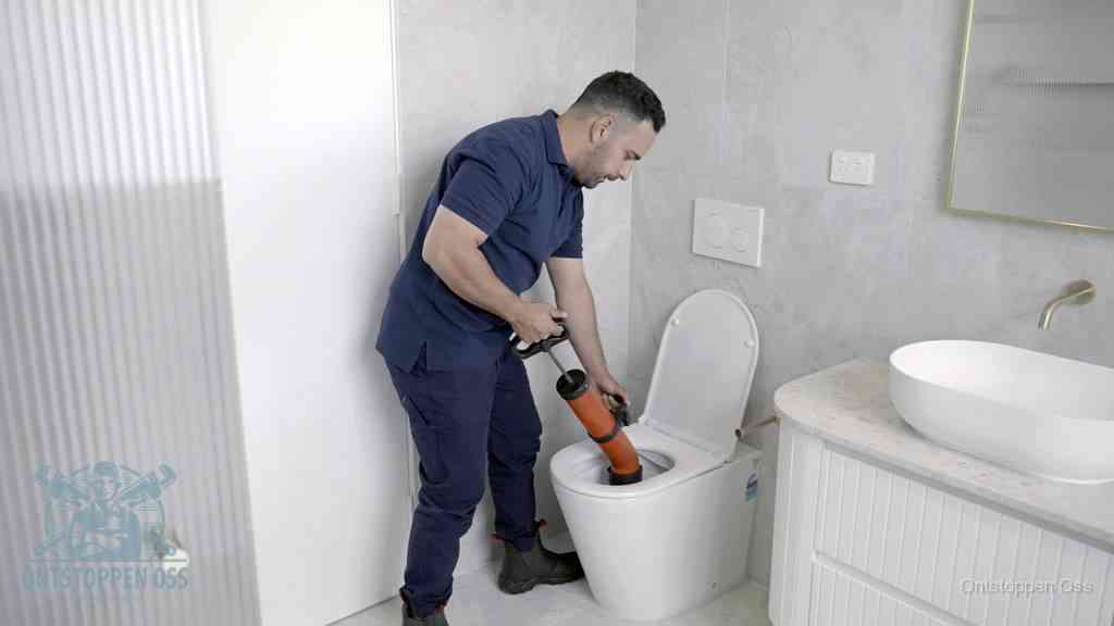 Een monteur buigt over een wandcloset en duwt met de hand een persluchtontstopper in de toiletpot om de verstopping handmatig los te maken in Oss