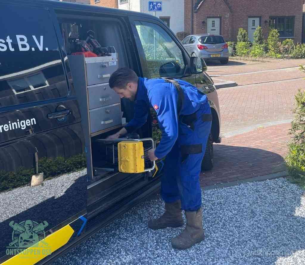 Een monteur pakt buiten op de oprit gereedschap uit de bedrijfsbus, het moment om een professional in te schakelen voor een verstopte afvoer in Oss