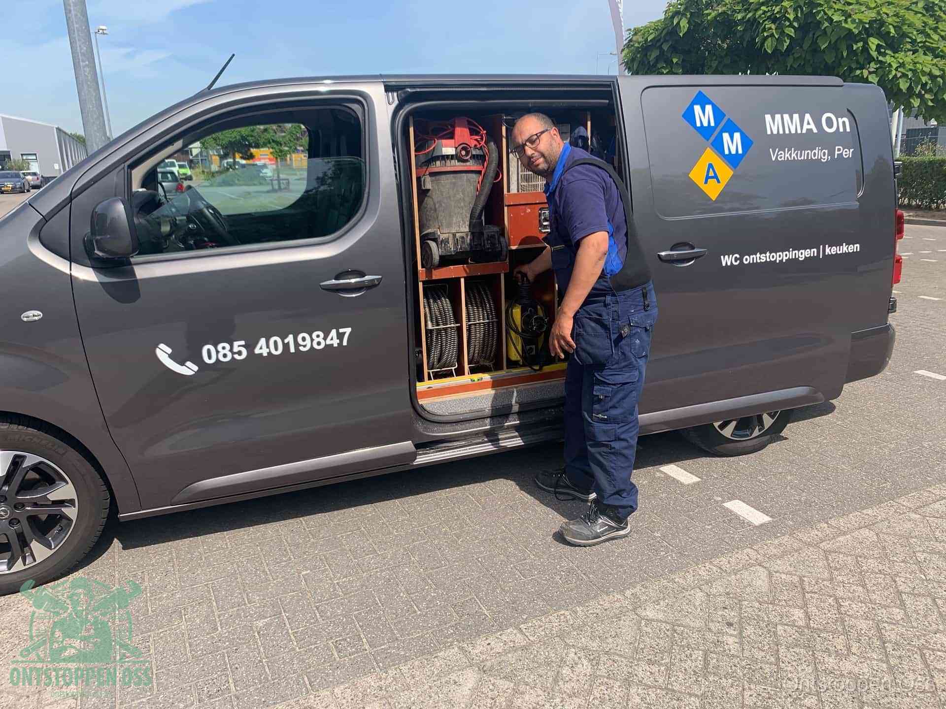 Een monteur bij de open schuifdeur van zijn bedrijfsbus op een parkeerplaats, klaar om de oorzaak van terugkerende afvoerverstoppingen aan te pakken in Oss