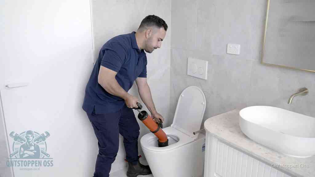 Een monteur gebruikt een handmatige perspomp (toiletontstopper) op een wandcloset tijdens het professioneel wc ontstoppen in Oss