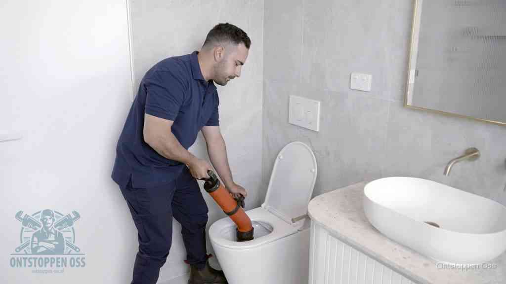 Een man gebruikt een handmatige luchtdruk-ontstopper in een modern betegeld toilet om zelf de wc te ontstoppen in Oss